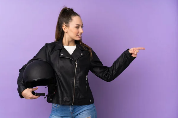 若いですブルネット女性とともにオートバイヘルメット上の隔離された紫色の背景を指す側に製品を提示します — ストック写真
