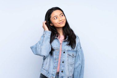 Genç Çinli bir kadın mavi arka planda izole edilmiş bir fikir düşünüyor.