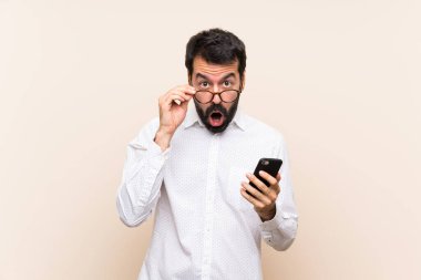 Sakallı genç adam cep telefonunu tutuyor ve şaşırıyor.