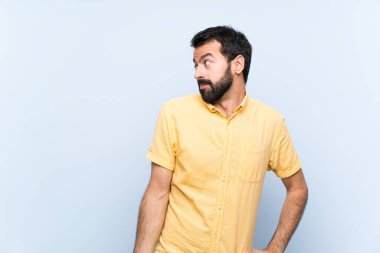 Mavi arka planda sakallı genç adam şüpheli hareketler yapıyor.