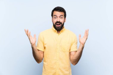 Sakallı genç bir adam soyutlanmış mavi arka plan ve şok olmuş yüz ifadesi.