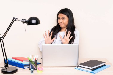 İş yerinde bej arka planda izole edilmiş dizüstü bilgisayarı olan Asyalı öğrenci ellerini öne uzatarak sinirlerini geriyor.