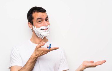 Adam sakalını soyutlanmış beyaz arka planda tıraş ediyor. Davet etmek için ellerini yana açıyor.