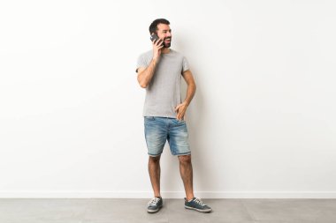 Sakallı yakışıklı bir adamın cep telefonuyla sohbet ederken tam boy fotoğrafı.