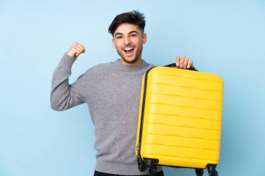 Arap yakışıklı adam mavi arka planda izole edilmiş seyahat valiziyle tatilde.