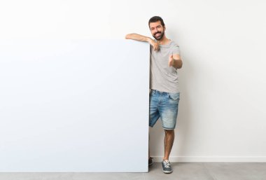 Sakallı genç yakışıklı adam büyük mavi boş bir levhayı tutuyor ve iyi bir anlaşma için el sıkışıyor.