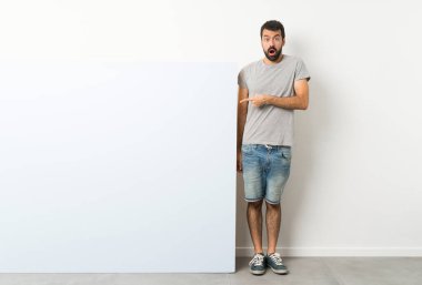 Sakallı genç, yakışıklı bir adam elinde kocaman, mavi, boş bir pankart tutuyor.