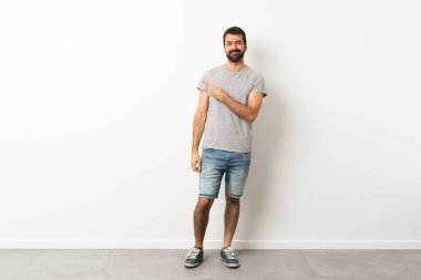 Sakallı yakışıklı bir adamın uzun bir resmi bir ürünü sunmak için kenarı işaret ediyor.