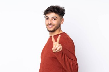 Arap yakışıklı adam izole edilmiş arka planda gülümsüyor ve zafer işareti gösteriyor.