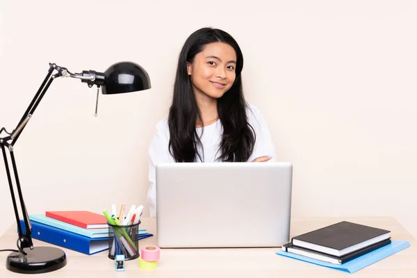 Student asian girl in a workplace with a laptop isolated on beige background happy and smiling