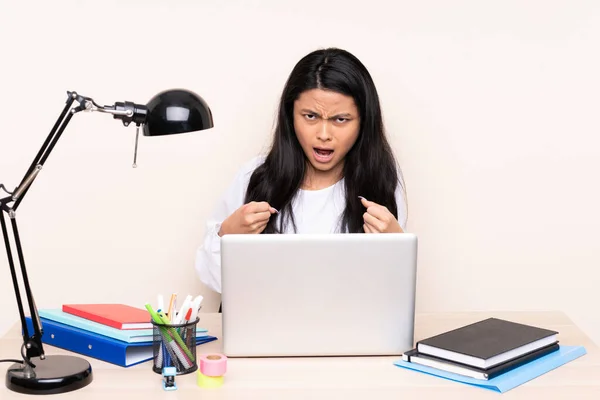 Student asian girl in a workplace with a laptop isolated on beige background frustrated by a bad situation