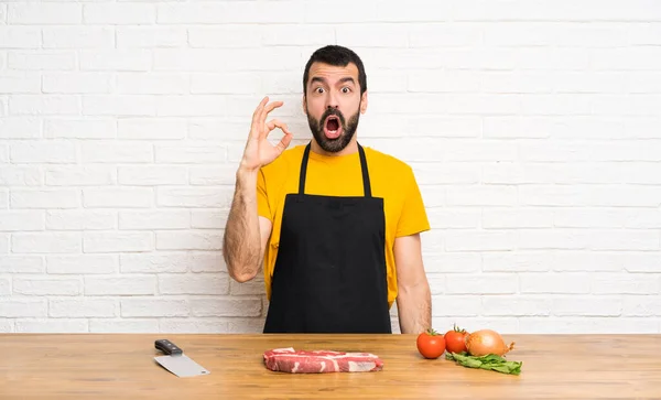 Chef holding in a cuisine surprised and showing ok sign