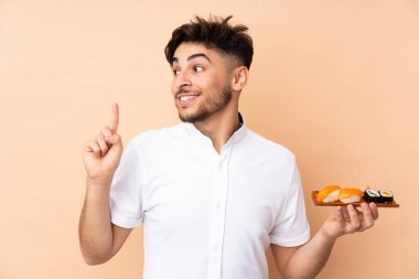 Bej arka planda izole edilmiş suşi yiyen Arap bir adam çözümü bulmak için parmağını kaldırıyor.