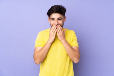 Arap yakışıklı adam izole edilmiş arka planda mutlu ve gülümsüyor elleriyle ağzını kapatıyor.