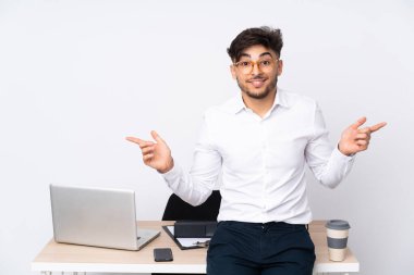 Beyaz arka planda izole edilmiş bir ofiste yaşayan Arap bir adam parmak uçlarını işaret ediyor ve mutlu.
