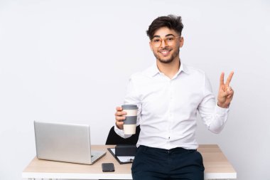 Beyaz arka planda izole edilmiş bir ofiste Arap bir adam zafer işaretini iki elle gösteriyor.