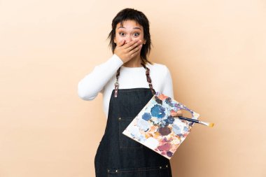 Arkaplanda palet tutan genç bir sanatçı sürpriz bir yüz ifadesiyle.