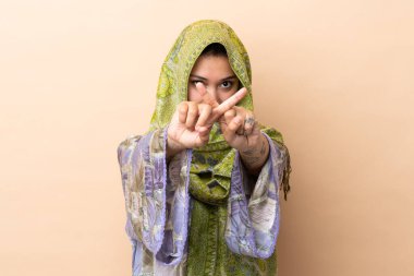 Hintli bir kadın bej arka planda izole edilmiş bir şekilde bir eylemi durdurmak için el hareketi yapıyor.
