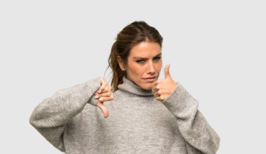 Balıkçı yakalı sarışın kadın iyiye kötüye işaret veriyor. İzole edilmiş gri arkaplan arasında kararsız