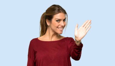 Sarışın kadın mavi arka planda mutlu bir ifadeyle selamlıyor.