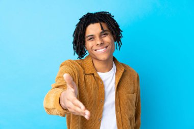 Kadife ceketli genç Afro-Amerikalı adam, iyi bir anlaşmadan sonra mavi arka planda el sıkışıyor.