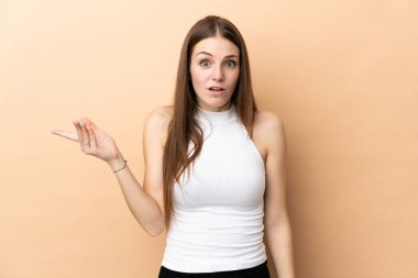 Beyaz tenli genç bir kadın, bej arka planda izole edilmiş, şüpheli hareketler yapıyor.