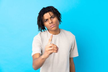 Genç Afro-Amerikan erkek, izole edilmiş mavi arka plan hayal kırıklığına uğramış ve ön tarafı işaret ediyor.