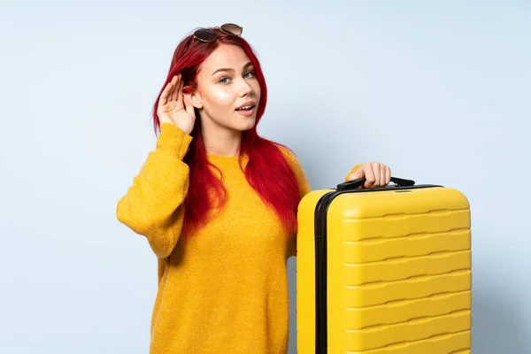 旅行的女孩拿着一只蓝色背景的手提箱 用手捂住耳朵听着什么 — 图库照片