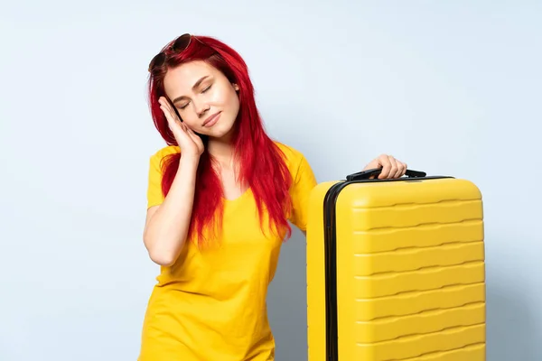 抱着一个蓝色背景的手提箱的旅行女孩 带着安稳的表情打盹 — 图库照片