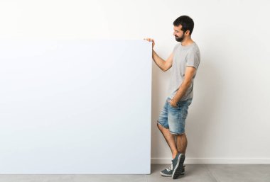 Sakallı, genç ve yakışıklı bir adam elinde kocaman mavi bir pankart tutuyor.