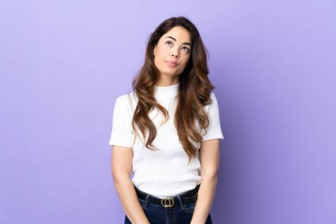 İzole edilmiş mor arka planı olan bir kadının yukarı bakarken şüpheleri var