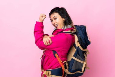 Pembe arka planda büyük bir sırt çantası olan genç dağcı kız güçlü bir jest yapıyor.