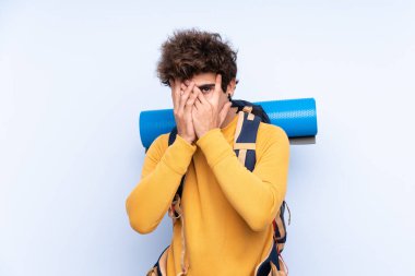 İzole edilmiş mavi arka planı olan büyük bir sırt çantasıyla genç dağcı gözlerini kapatıp parmaklarından bakıyor.