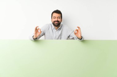 Sakallı, genç, yakışıklı bir adam. Zen pozisyonunda yeşil, boş bir levha tutuyor.