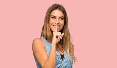 Kot elbiseli sarışın kadın izole edilmiş pembe arka planda sessizlik işareti gösteriyor.