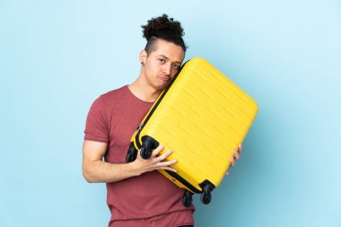 İzole edilmiş mavi geçmişi olan beyaz bir adam seyahat valiziyle tatilde ve mutsuz.