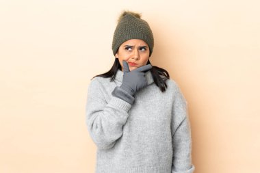 Kışlık şapkalı genç Kolombiyalı kız bej arka planda izole edilmiş bir fikir düşünüyor.