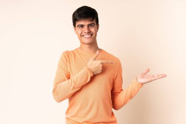 İzole edilmiş bej arkaplanda yakışıklı bir adam. Avucunun içinde bir reklam koymak için hayali bir alan tutuyor.