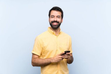 Mavi arka planda sakallı genç bir adam cep telefonuyla mesaj gönderiyor.