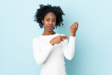 Genç Afrikalı Amerikalı kadın mavi arka planda izole edilmiş, geç kalma jesti yapıyor.