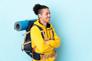İzole edilmiş mavi arka planda büyük bir sırt çantası olan genç dağcı.
