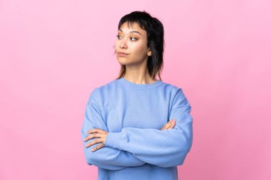 Genç Uruguaylı kadın pembe arka planda kollarını kavuşturuyor.