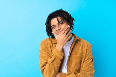 Kadife ceketli genç Afrikalı Amerikalı bir adam izole edilmiş mavi arka planda bir fikir düşünüyor.