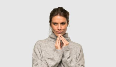 Blonde woman with turtleneck scheming something over isolated grey background clipart