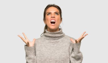 Sarışın, balıkçı yaka kazaklı bir kadın. Gri arka planda kötü bir durum yüzünden hayal kırıklığına uğramış.