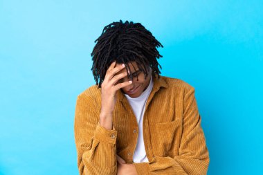 Kadife ceketli genç Afro-Amerikalı adam mavi arka planda gülüyor.