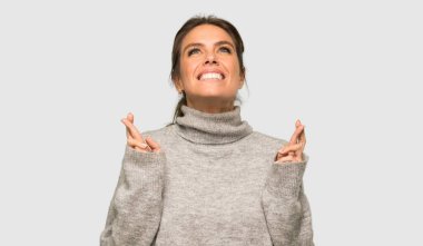 Parmakları geçiş ve izole gri arka plan üzerinde en iyi dilek ile balıkçı yaka ile Sarışın kadın