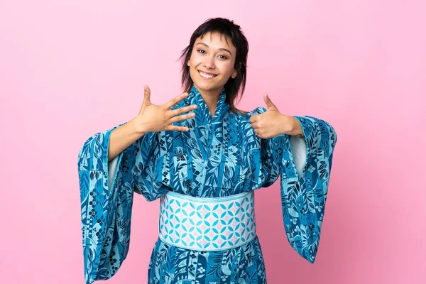 Young woman wearing kimono over isolated blue background counting six with fingers