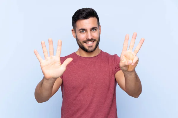 Sakallı Genç Yakışıklı Bir Adam Mavi Arka Planda Parmaklarıyla Sekiz — Stok fotoğraf