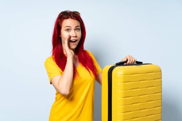 旅行的女孩拿着一个蓝色背景的手提箱 指着旁边展示一个产品 低声说了些什么 — 图库照片